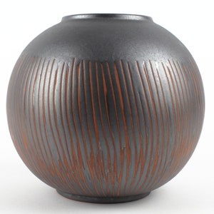 Peut inclure: Un vase rond en céramique noire avec une surface texturée. Le vase a un glaçage brun qui crée un motif rayé.