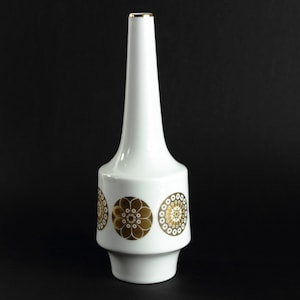 May include: White ceramic vase with a gold rim and gold geometric designs. The vase has a narrow neck and a wide base.