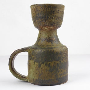 Könnte beinhalten: Ein grüner Kerzenhalter aus Keramik mit einem Griff. Der Halter hat eine strukturierte Oberfläche und eine braune Glasur.