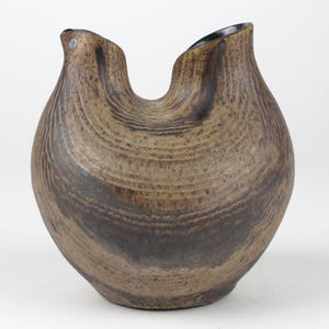 May include: A brown ceramic vase with a unique, organic shape. The vase has a wide, rounded body and two upward-curving spouts, creating a distinctive silhouette. The surface features a textured, wood-grain-like pattern. The vase is approximately 8 inches tall.