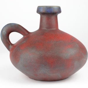 Könnte beinhalten: Eine rote und blaue Keramikvase mit rundem Körper und Henkel. Die Vase hat eine gefleckte Glasur in Rot-, Blau- und Grautönen.