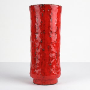 Peut inclure: Un vase en céramique rouge, de forme cylindrique et haute. La surface est texturée, avec des éclats sombres dans le vernis rouge. Le vase a un léger évasement en haut et une petite base ronde. Un objet décoratif pour la maison.