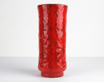 May include: A tall, cylindrical red ceramic vase with a textured surface. The vase has a slightly flared top and a small, round base. The red glaze has dark speckles throughout, adding visual interest. A decorative piece for home decor.