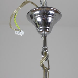 May include: Close-up of a chrome-finished ceiling light fixture. The fixture has a bell-shaped canopy, a central rod, and a chain. Electrical wiring with a white connector is visible. The light fixture is suspended from a metal hook.
