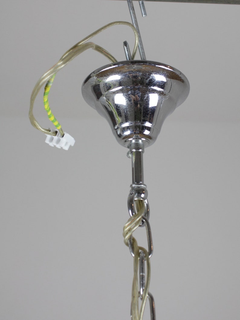 May include: Close-up of a chrome-finished ceiling light fixture. The fixture has a bell-shaped canopy, a central rod, and a chain. Electrical wiring with a white connector is visible. The light fixture is suspended from a metal hook.