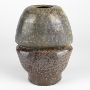 May include: A two-toned ceramic vase with a bulbous top and a flared base. The top section is a mottled gray-green with gold flecks, while the base is a speckled brown. The vase has a unique, organic shape and a glossy finish.