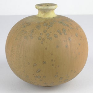 May include: A round, light brown ceramic vase with a speckled glaze. The vase has a small opening at the top.