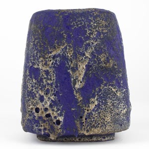 May include: A blue and beige ceramic vase with a textured, rough surface. The vase has a wide base and a cylindrical shape, with a slightly flared top. The color is a deep blue with beige and black accents.
