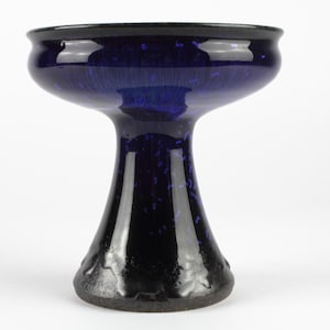 Op de afbeelding: Een diep kobaltblauwe keramische schaal op voet met een brede, uitlopende rand en een taps toelopende basis. Het glanzende oppervlak heeft een subtiel, donkerblauw gespikkeld patroon over het hele lichaam, uitlopend in een effen donkere voet.