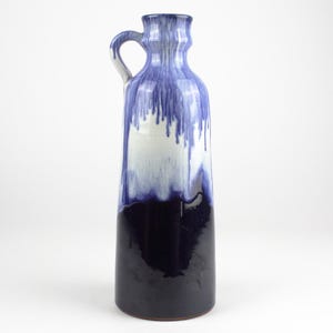 May include: A tall, blue and white ceramic vase with a drip glaze design. The vase has a wide mouth and a handle.