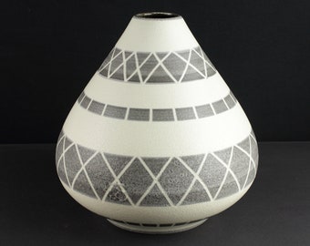 Può includere: Un vaso in ceramica bianca con un motivo geometrico grigio. Il vaso ha una base larga e un collo stretto.