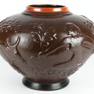 以下が含まれることがあります： 人物と葉のレリーフ模様が施された茶色の陶器の花瓶。花瓶は濃い茶色の釉薬がかけられ、縁は赤色です。