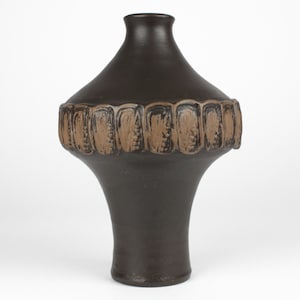 Può includere: Un vaso in ceramica marrone scuro dalla forma unica. Il vaso ha un corpo ampio e arrotondato con una fascia strutturata di rettangoli marroni. Si restringe verso un collo stretto e una base svasata. Un oggetto decorativo per la casa.