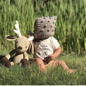 May include: A crocheted deer plush toy with a matching hat and a white onesie with the text "Sweeter than Little Berries". The deer is tan with brown accents. The hat is tan with dark brown bobbles.