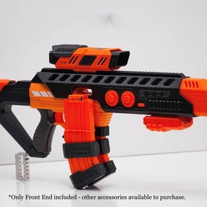 Op de afbeelding: Een zwart en oranje speelgoedpistool met een richtkijker en meerdere magazijnen die eraan zijn bevestigd. Het pistool heeft een zwarte greep en een zwarte loop. Het pistool is gemaakt van plastic en heeft een realistisch ontwerp.