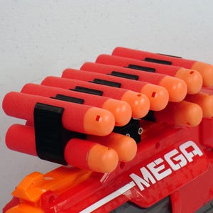 Puede incluir: Una pistola de juguete Nerf Mega roja y naranja con un clip negro que sostiene múltiples dardos naranjas.