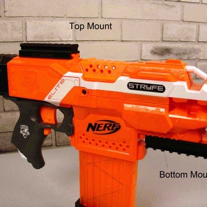 Könnte beinhalten: Eine orange-schwarze Nerf Stryfe Spielzeugpistole mit einem weißen Streifen und den Worten "Elite" und "Stryfe" auf der Seite. Die Pistole hat eine schwarze Obermontage und eine schwarze Untermontage.