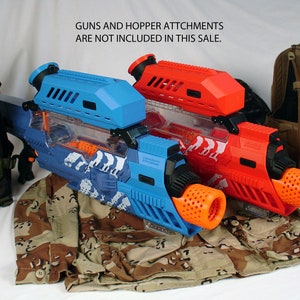 May include: Two Nerf blasters, one blue and one red, with a camouflage pattern and orange barrels.  The text "GUNS AND HOPPER ATTCHMENTS ARE NOT INCLUDED IN THIS SALE." is visible in the image.
