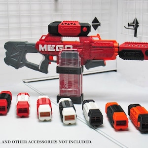 Op de afbeelding: Zeven rode, witte en zwarte plastic magazijnverlengingen voor een Nerf-blaster. De verlengingen zijn in een rij op een wit oppervlak gerangschikt. *BLASTER EN ANDERE ACCESSOIRES ZIJN NIET INBEGRIPPEN.*