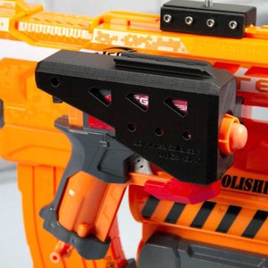 Op de afbeelding: Een zwart 3D-geprint accessoire voor een Nerf-pistool. Het accessoire is aan de zijkant van het pistool bevestigd en heeft een textuur. De tekst "2D Blaster Designs" en "3D Printed" is zichtbaar op het accessoire.