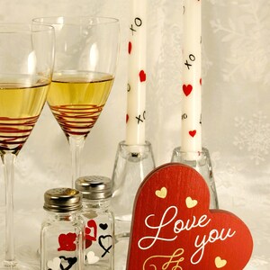 white candles with red hearts and black xo beside two wine glasses