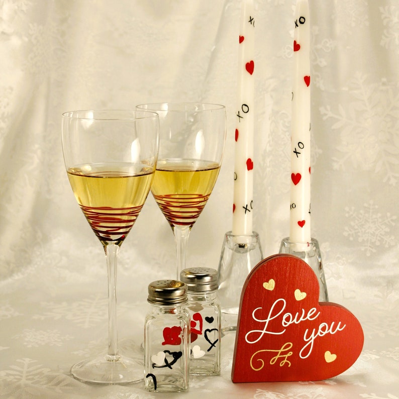 white candles with red hearts and black xo beside two wine glasses