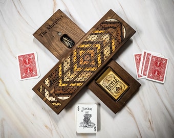 May include: A wooden cribbage board with a personalized inscription "The Murphys" and a deck of playing cards. The board has a dark wood finish and features a traditional cribbage board design with a start position and a scoring track. The playing cards are standard playing cards with a red back.