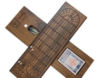May include: A personalized wooden cribbage board with a card holder and a slot for pegs. The board is engraved with "The Parvan 05.29.2022".