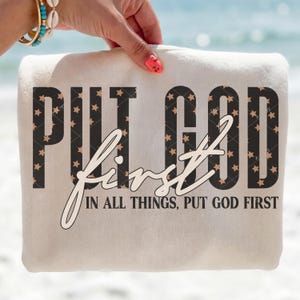 Puede incluir: Un artículo de tela plegado de color crema con las palabras "PUT GOD first" en negrita, negro, lleno de patrones de estrellas. La palabra "first" está escrita en cursiva. La frase "IN ALL THINGS, PUT GOD FIRST" está debajo.