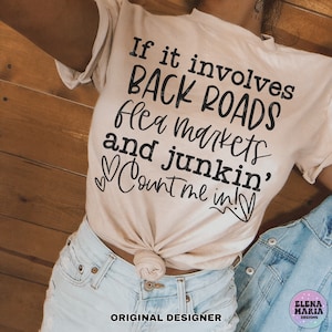 May include: A beige t-shirt with the text "If it involves BACK ROADS flea markets and junkin', Count me in!" printed in black. The shirt is being worn by a person with blue jeans. The text "ORIGINAL DESIGNER" is printed below the shirt.