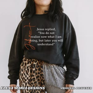 May include: Black sweatshirt with the text "Jesus replied, 'You do not realize now what I am doing, but later you will understand'" in white. The word "John 13:7" is written in orange. The bottom of the image shows animal print and checkered pants.