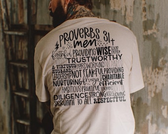 Op de afbeelding: Een wit T-shirt met zwarte tekst die "Spreuken 31+ mannen" luidt en een reeks positieve karaktereigenschappen opsomt.
