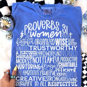 May include: A blue t-shirt with the words "PROVERBS 31 Women" in white script. The shirt also lists several positive attributes such as "faithful", "organized", and "wise". The shirt is surrounded by disco balls and a black and white checkered pattern.