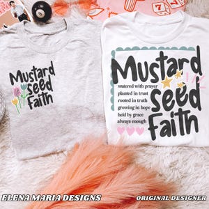Puede incluir: Dos camisetas con la frase "Mustard Seed Faith" estampada. Una es gris claro con detalles florales, y la otra es blanca con un borde decorativo y texto adicional sobre la fe. Las camisetas est&aacute;n sobre una superficie esponjosa de color melocot&oacute;n.