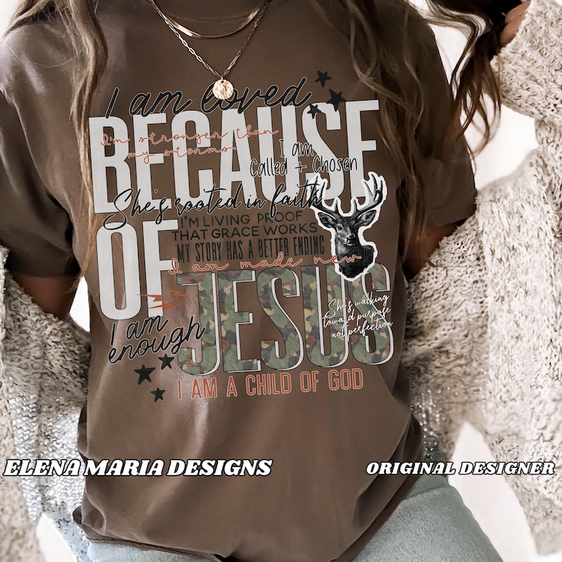 May include: A brown t-shirt with the words "I am loved because of Jesus" in white and camouflage lettering. The shirt features a deer graphic and additional text, including "I am a child of God."