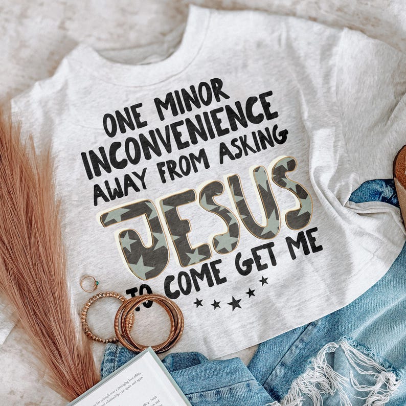 Pode incluir: Uma t-shirt cinza mesclado claro com texto preto que diz ONE MINOR INCONVENIENCE AWAY FROM ASKING JESUS TO COME GET ME. A palavra JESUS est&aacute; impressa em uma fonte grande e em negrito com um padr&atilde;o de estrelas verde escuro e claro.