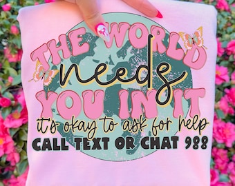 May include: A light pink sweatshirt with the text "THE WORLD needs YOU IN IT" in pink and black lettering. The sweatshirt also includes the text "it's okay to ask for help" and "CALL TEXT OR CHAT 988". Two butterfly graphics are also included.