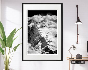 May include: A black and white photograph of a mountain range with clouds in the background. The photo is framed in a black frame and is hanging on a white wall.