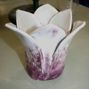 May include: A ceramic tulip-shaped vase, handmade with a white exterior and a purple, mottled pattern on the lower section. The interior is white. The design mimics a blooming tulip flower, suitable for home decor.