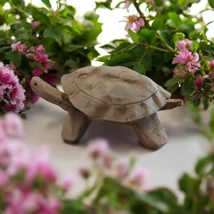 May include: A hand-crafted clay turtle figurine with a brown glaze. The turtle is walking on a white surface with pink flowers in the background.