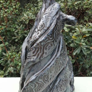 May include: A tall, hand-sculpted ceramic figurine of a howling wolf with a glossy, dark blue-grey glaze. The surface features intricate, raised swirling patterns and textured details that wrap around the body, emphasizing the wolf's form.