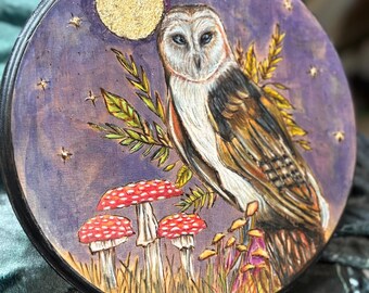 May include: A round wooden plaque with a painted image of a barn owl perched on a branch with mushrooms and a full moon in the background. The owl is brown, white, and black with yellow eyes. The moon is gold and the background is purple with gold stars.