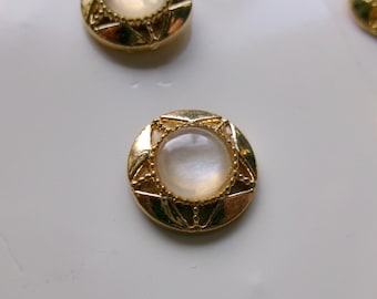 May include: Close-up of several gold-colored buttons with a pearlescent center. The buttons have a decorative, star-like design around the edges. The buttons are round and appear to be made of metal.