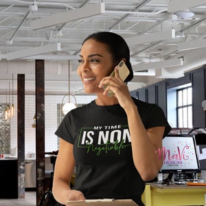 May include: A black t-shirt with the text "MY TIME IS NON-NEGOTIABLE" in green lettering. The shirt is being worn by a person in a modern office setting.