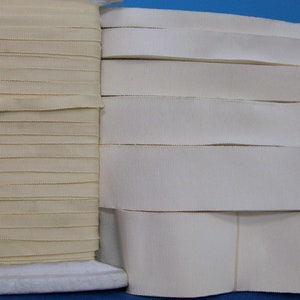May include: Two spools of off-white grosgrain ribbon. The ribbon on the left is folded and the ribbon on the right is stacked.