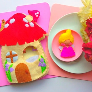 May include: A felt mushroom house with a red cap and white spots, a snail, and a felt fairy doll with a yellow head and pink dress. The house has a beige body with a door and window. The fairy is on a pink plate.