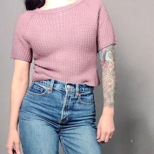 May include: A mauve waffle knit cropped sweater with short sleeves. The sweater is worn with high-waisted blue jeans.