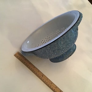 May include: A blue and white enamel colander with a speckled blue finish and a white interior. The colander has a handle on each side and a round base.