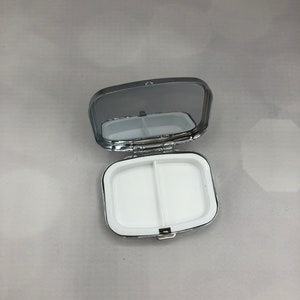 K&ouml;nnte beinhalten: Eine silberne Pillendose mit einem Spiegel auf dem Deckel. Die Dose hat zwei F&auml;cher f&uuml;r Pillen.