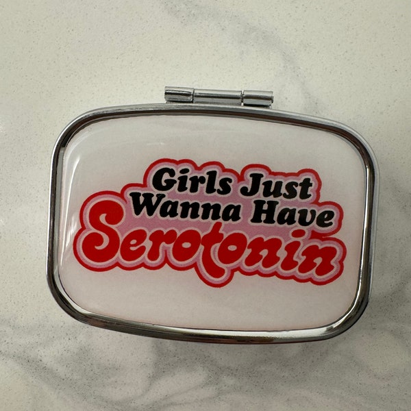 May include: A silver pill box with a white background and the text "Girls Just Wanna Have Serotonin" in red and pink lettering.